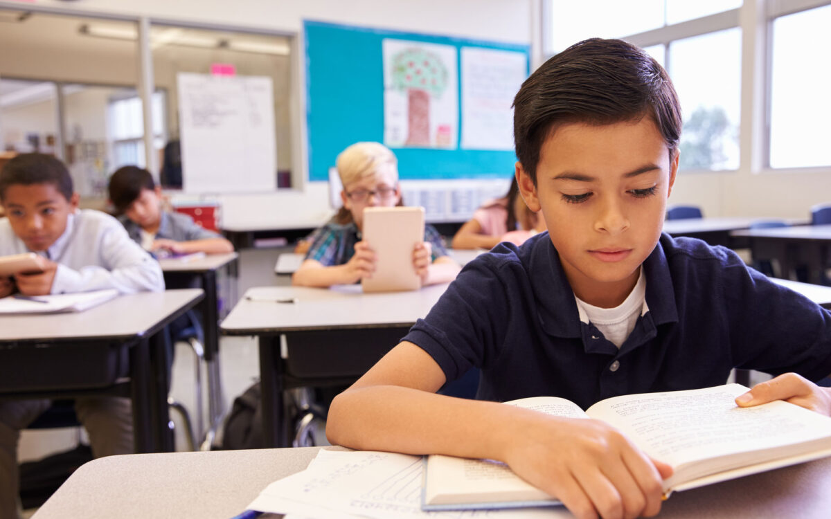 Student highlighting a passage in a workbook while a teacher points to the board during a lesson on author's purpose
